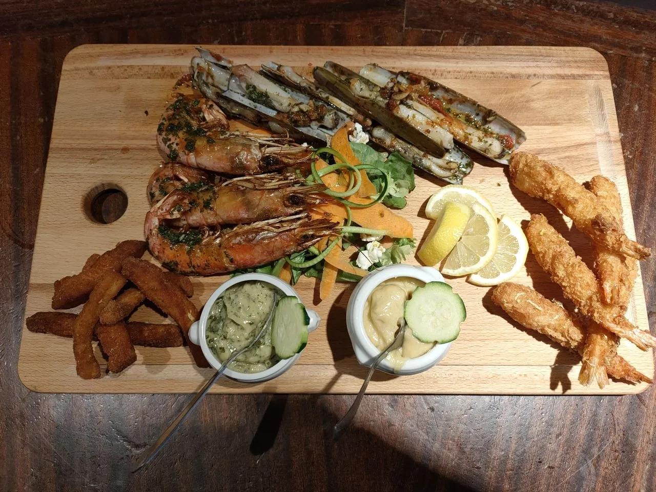 Pareillade de la mer servie sur une planche en bois avec crevettes, coquillages et sauces.