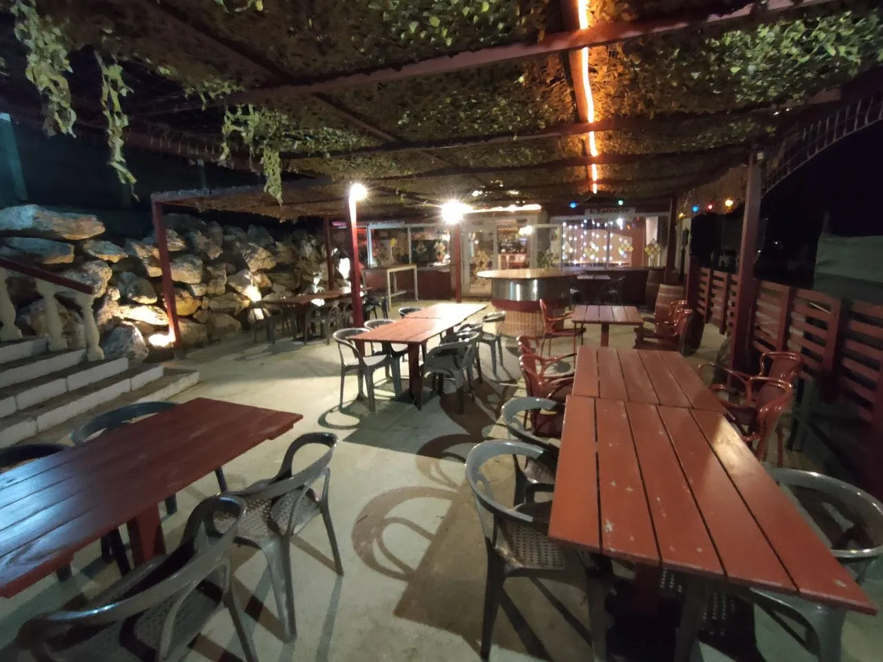 Terrasse couverte de Mont Relais Gaillard éclairée le soir, avec tables en bois et mur de pierres.