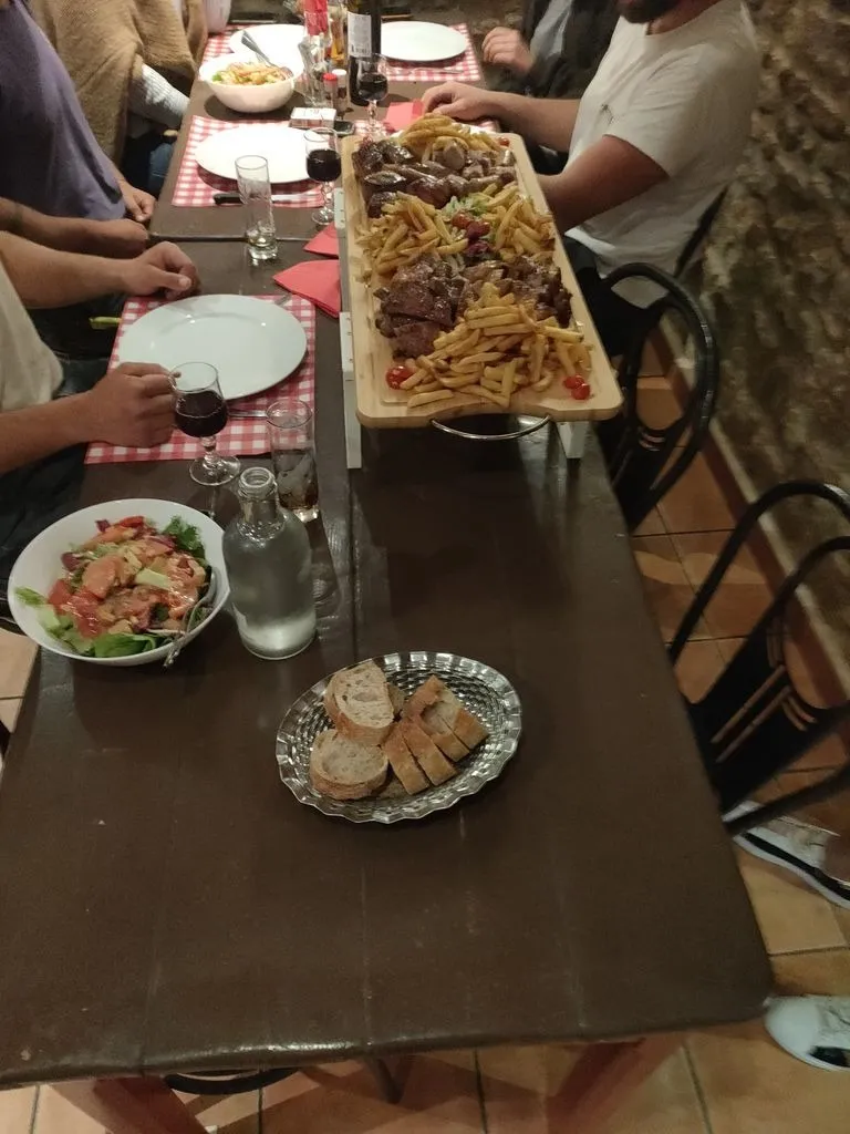 Grande planche de viandes grillées et de frites servie au milieu d’une table de convives.