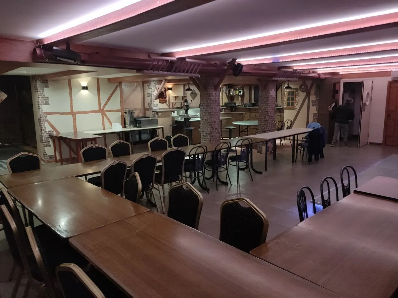 Salle de réception de Mont Relais Gaillard aménagée avec de longues tables et un éclairage rose.