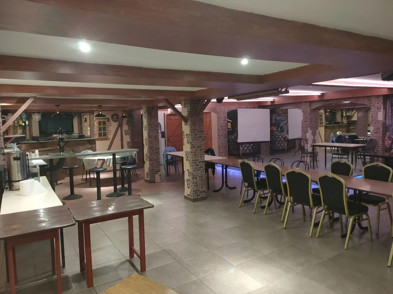 Salle de réception de Mont Relais Gaillard, avec tables, poutres en bois, grand écran et espace bar.
